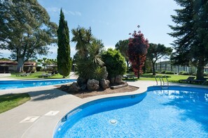 Une piscine dont le bord est revêtu de carrelage, entourée d’un jardin aménagé avec différents arbres et arbustes.