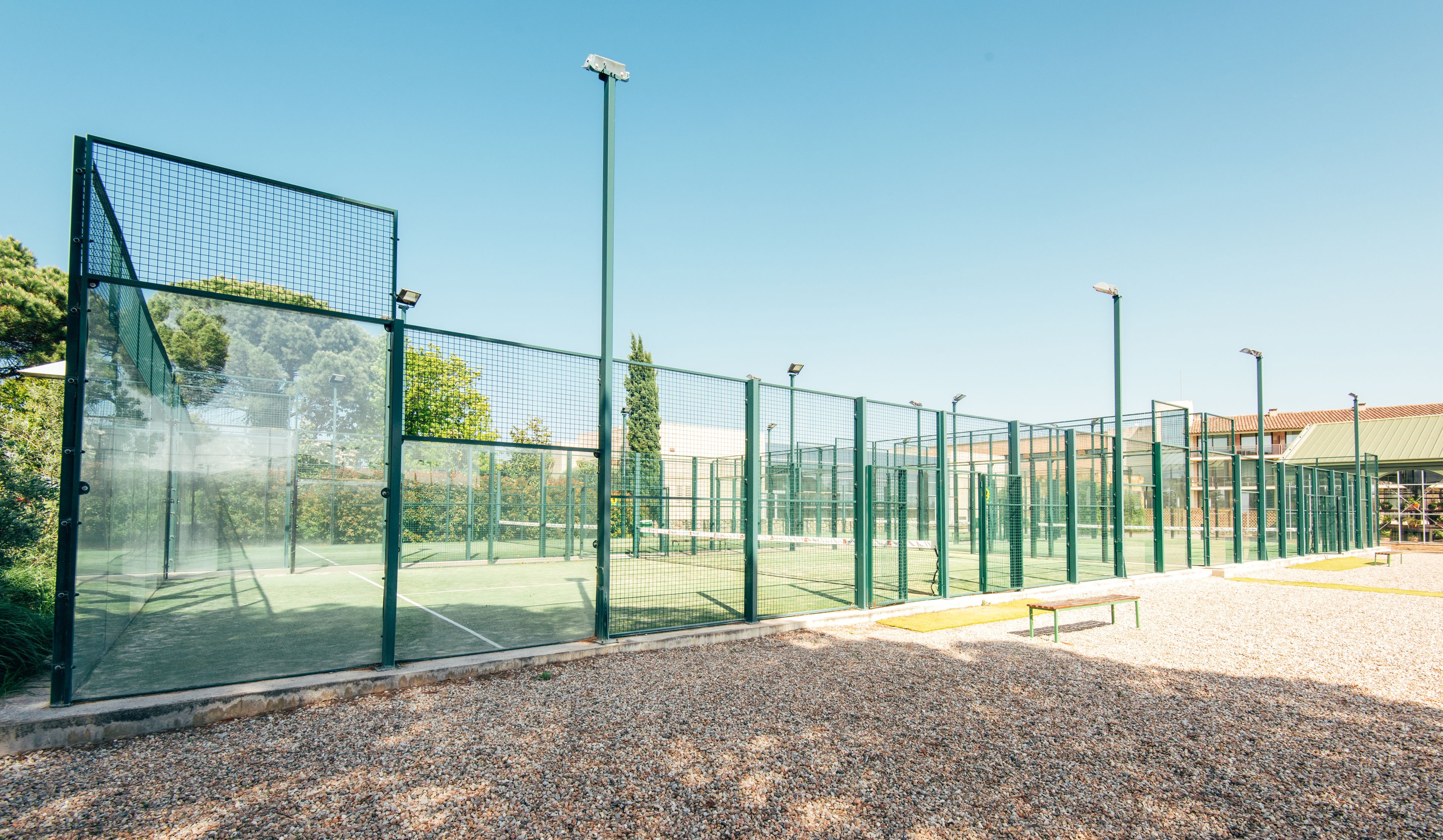 A tennis court with a green fence, a bench, and a gravel path.