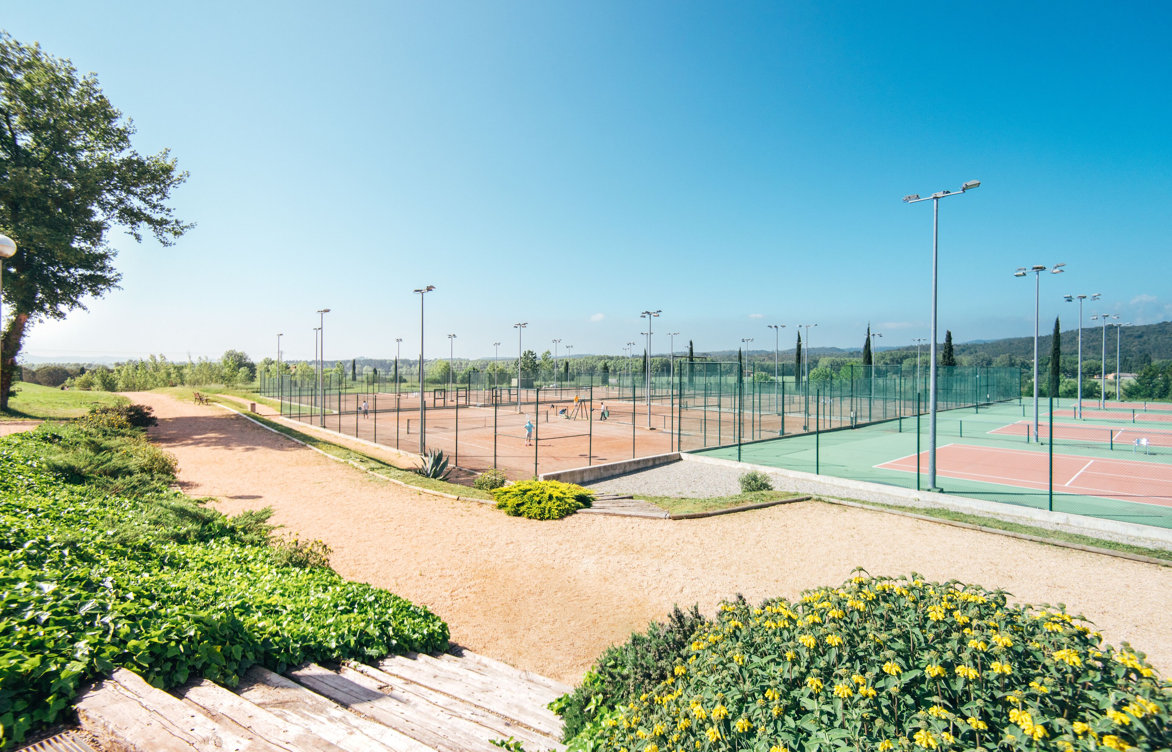 Una cancha de tenis con una valla, árboles y cielo despejado.