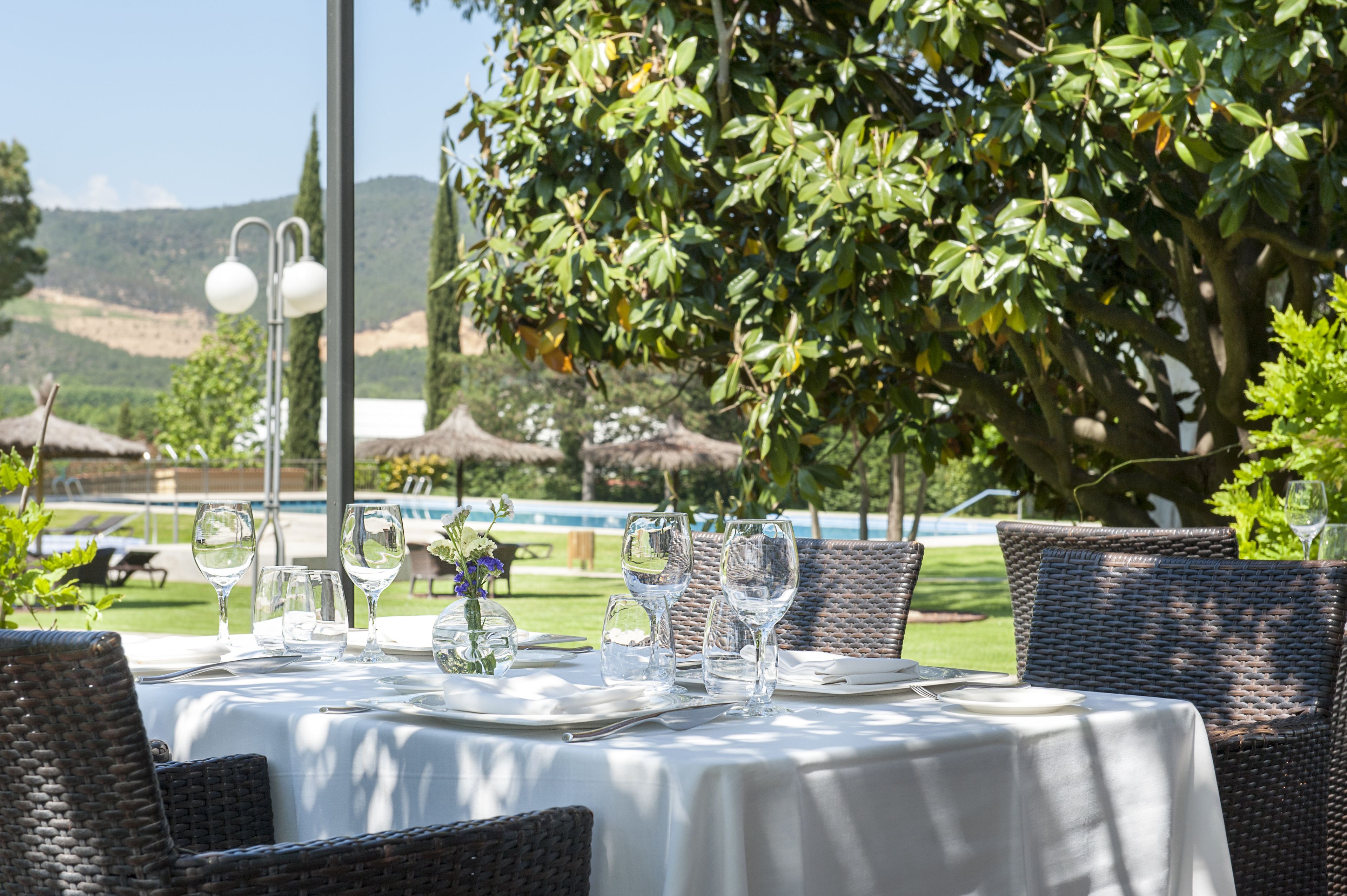 Un espacio de comedor al aire libre con sillas de mimbre y una mesa lista para una comida, con vistas a una piscina y follaje.