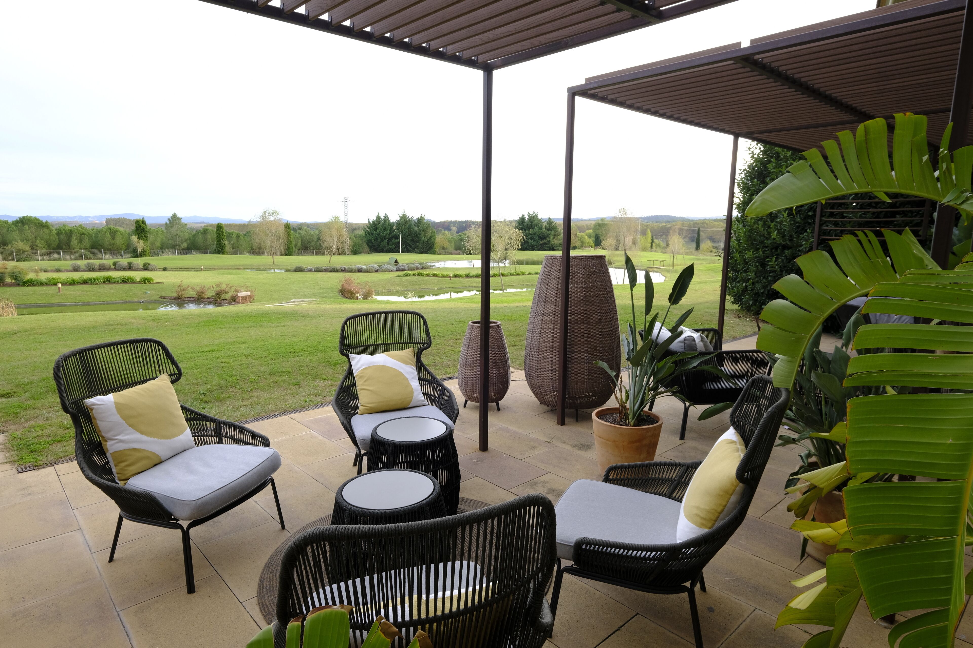 Une terrasse extérieure aménagée avec des meubles en osier, une pergola et une vue sur un paysage verdoyant.