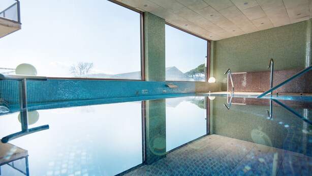 A clear indoor swimming pool with a glass floor, large windows, and a view of mountains. - Hotel Mas Solà (Santa Coloma de Farners)