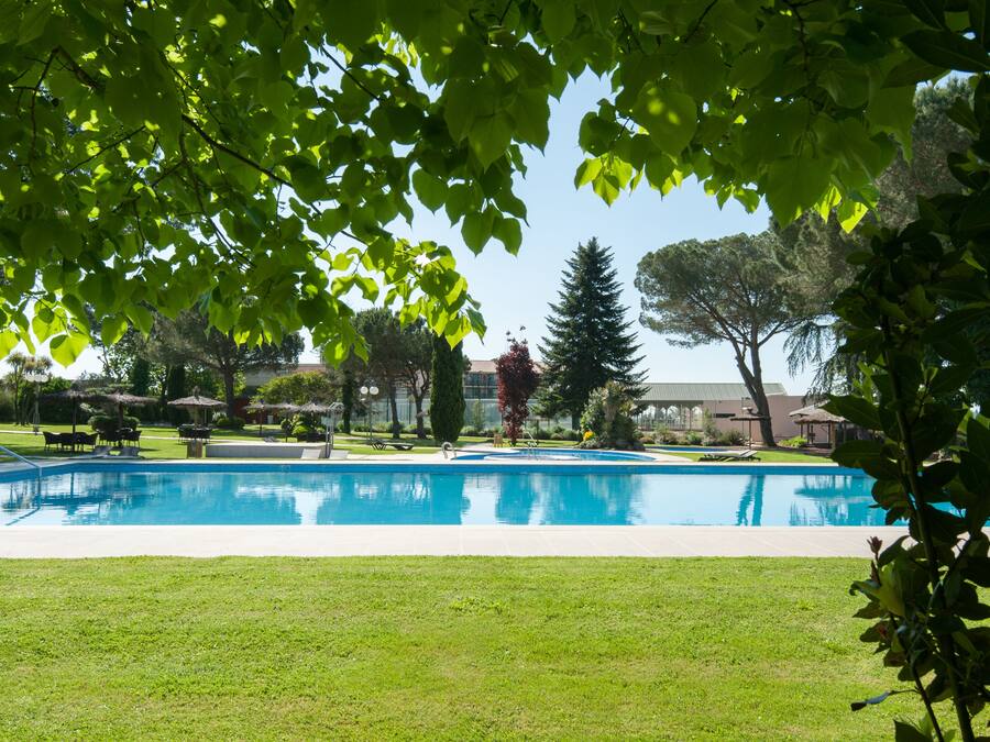 A swimming pool surrounded by grass, trees, and outdoor furniture.
