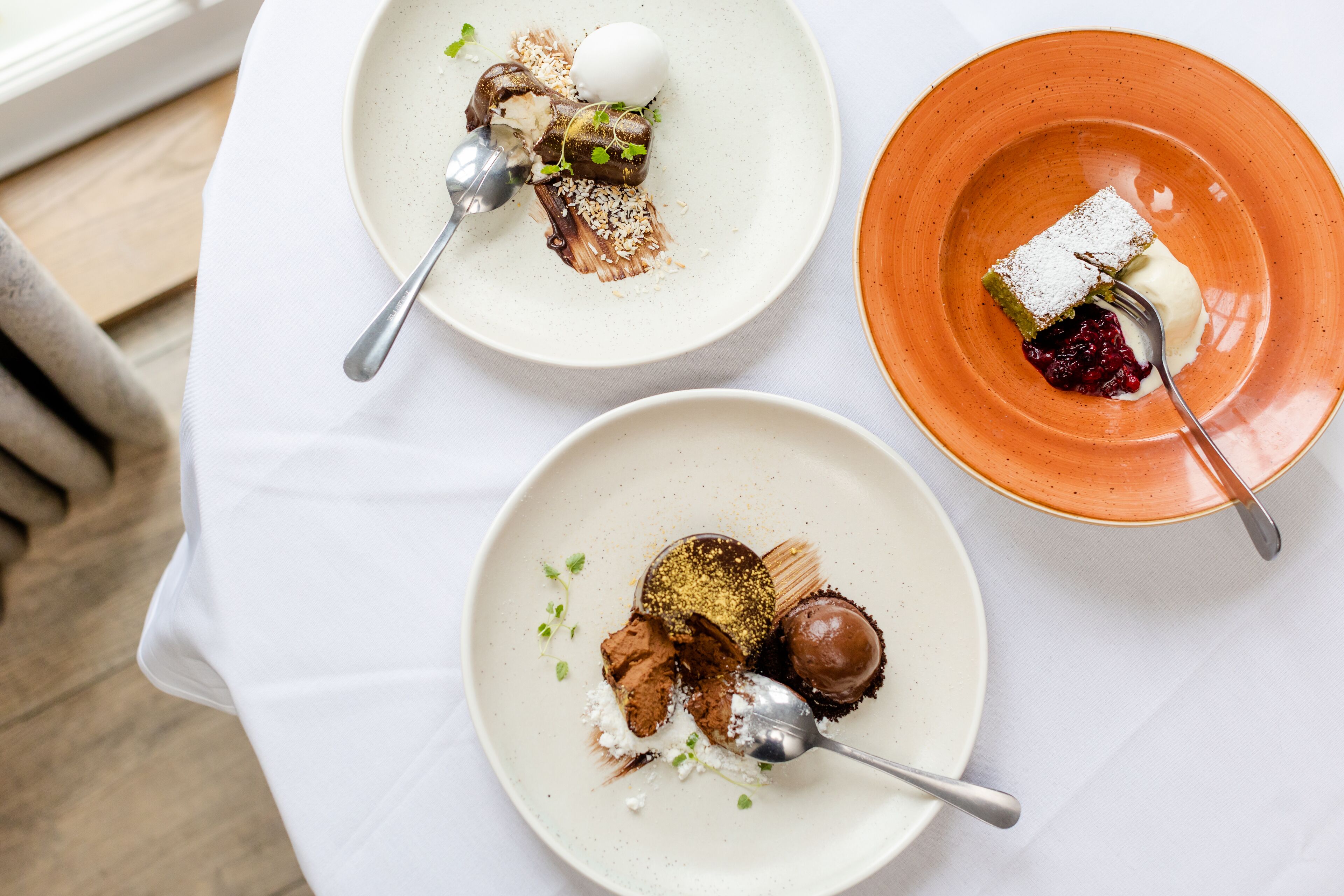 Three plates of dessert on a white tablecloth.