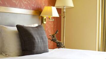 A hotel room with a bed, pillows, a lamp, and a wall-mounted light fixture.