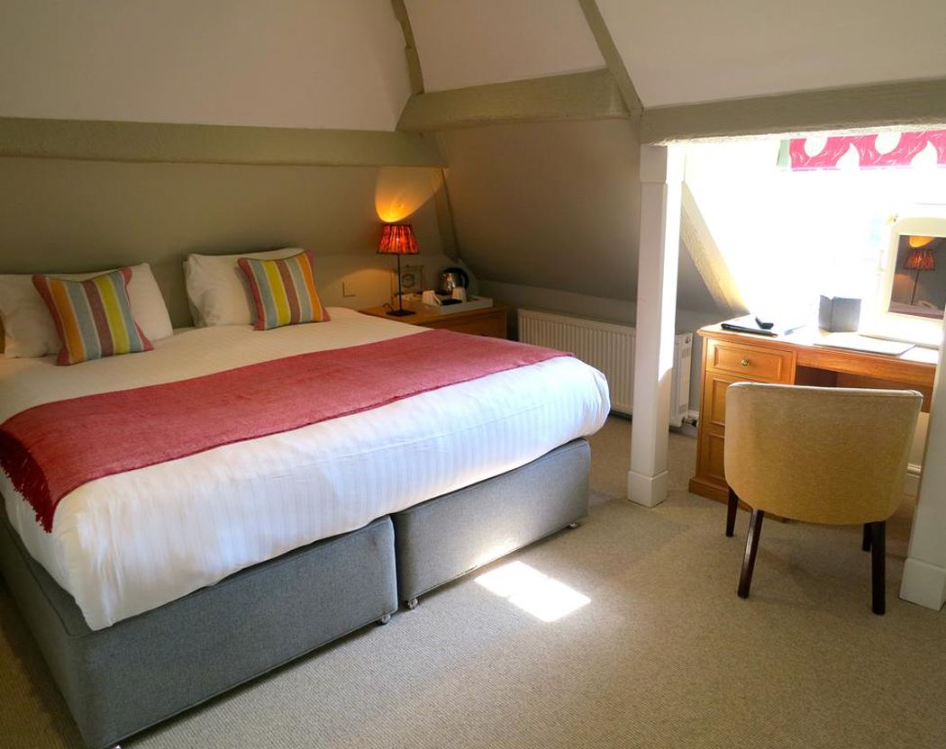 A bedroom with a bed, bedside table, lamp, chair, and a view of the outside.