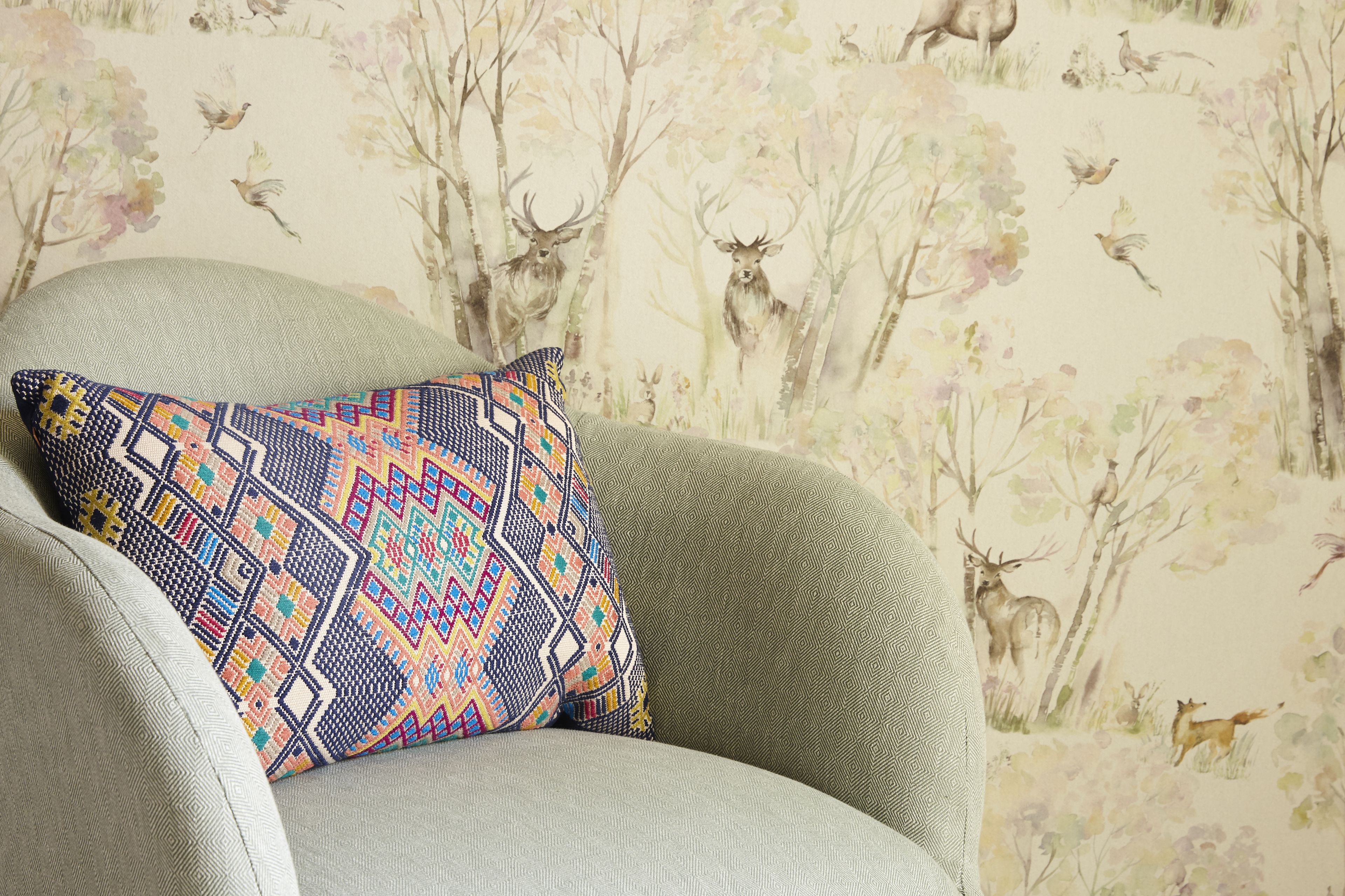 A chair with a patterned pillow and a wallpaper depicting deer and birds.