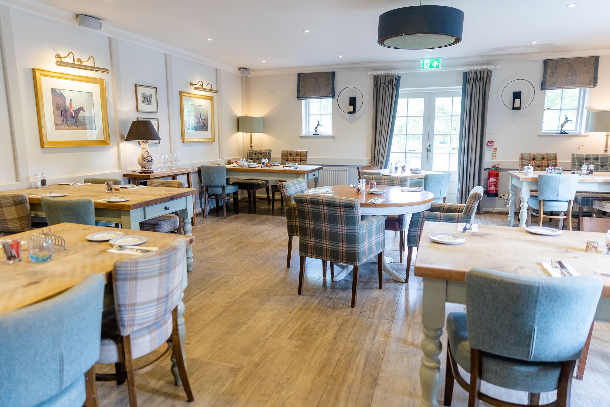 A dining area with multiple tables and chairs, framed pictures on the walls, and a large window with curtains.
