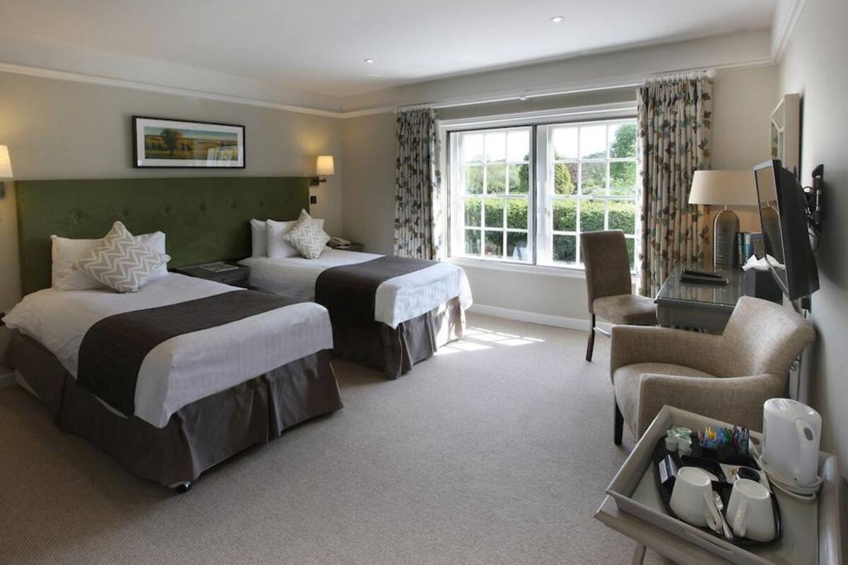 A hotel room with two beds, a chair, a desk, and a window with curtains.