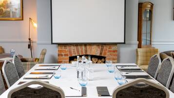 A conference room with a white table, grey chairs, a fireplace, and a projector screen.