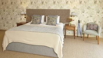 A neatly made bed with a grey headboard and patterned pillows, a small bedside table with a lamp, and a chair with a patterned cushion.