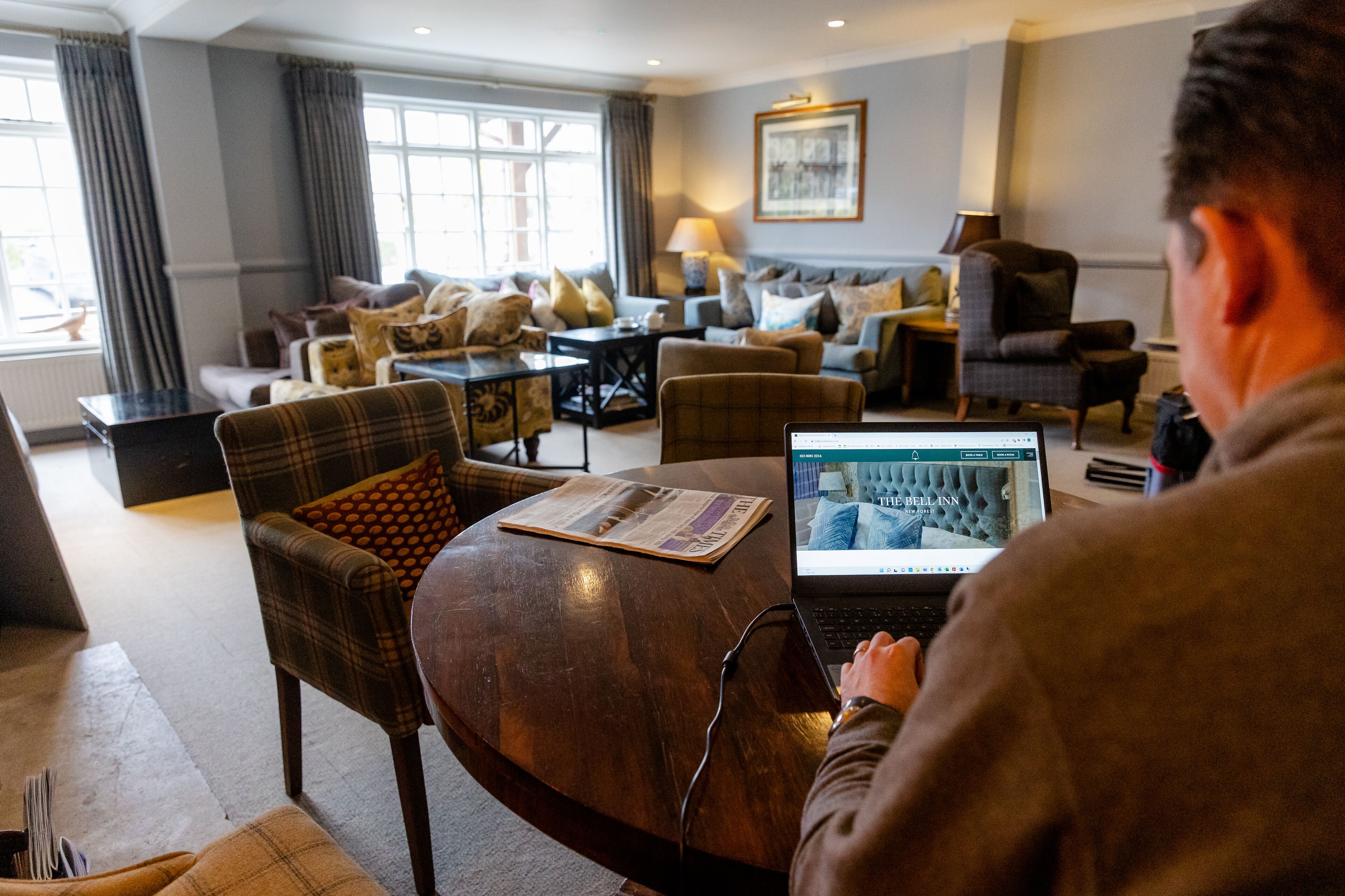 A hotel room with a modern interior, featuring a sofa set, a dining table, and a laptop on the table.