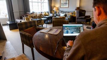 A hotel room with a modern interior, featuring a sofa set, a dining table, and a laptop on the table.