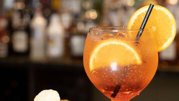Ein Cocktailglas mit Orangenscheibe und Strohhalm, dazu eine Schale Chips auf einer Bar.