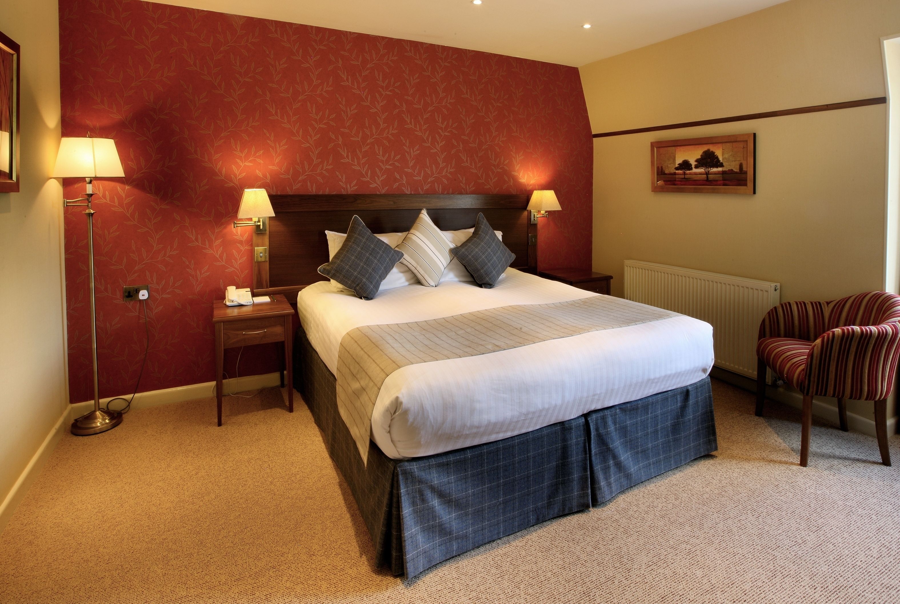 A hotel room with a large bed, two bedside lamps, a nightstand, a chair, and a radiator.