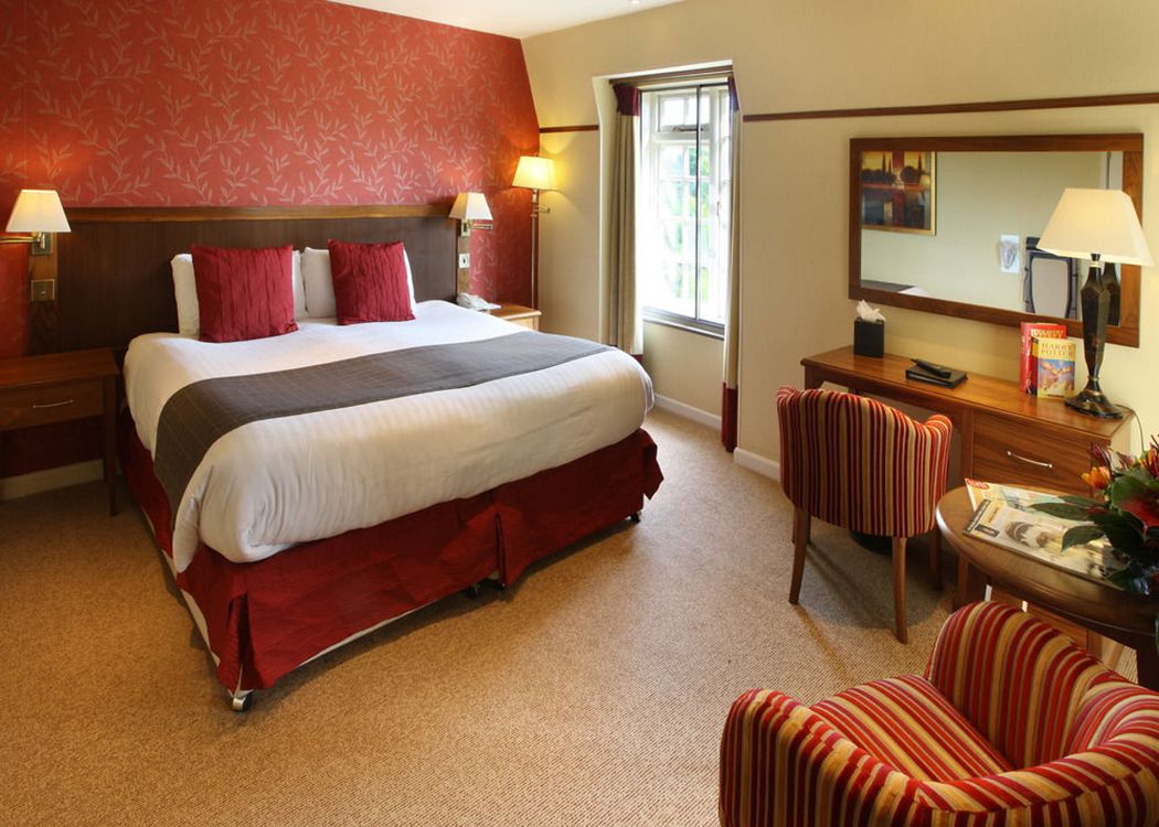 A hotel room with a large bed, a desk, two chairs, a mirror, and a window.