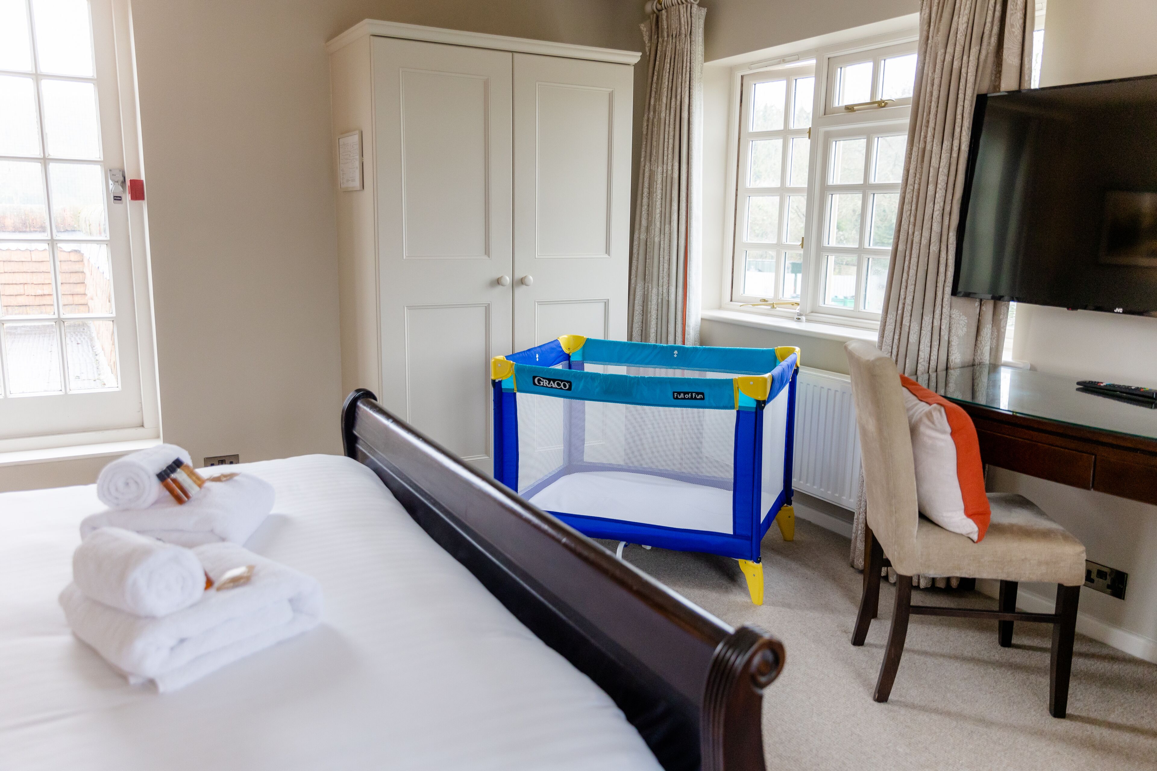 Een hotelkamer met een bed, een kinderbedje, een bureau en een televisie.