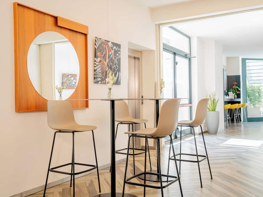 Um interior moderno com um espelho redondo, arte abstrata e uma área de refeições com cadeiras e uma mesa.
