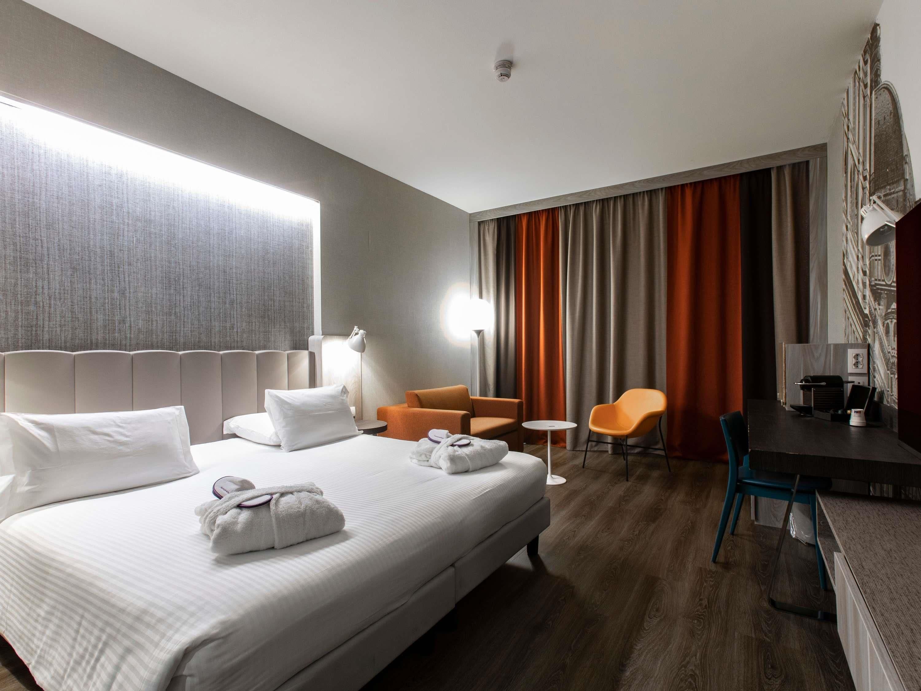 A hotel room with a large bed, two armchairs, a small table, and a desk with a chair.