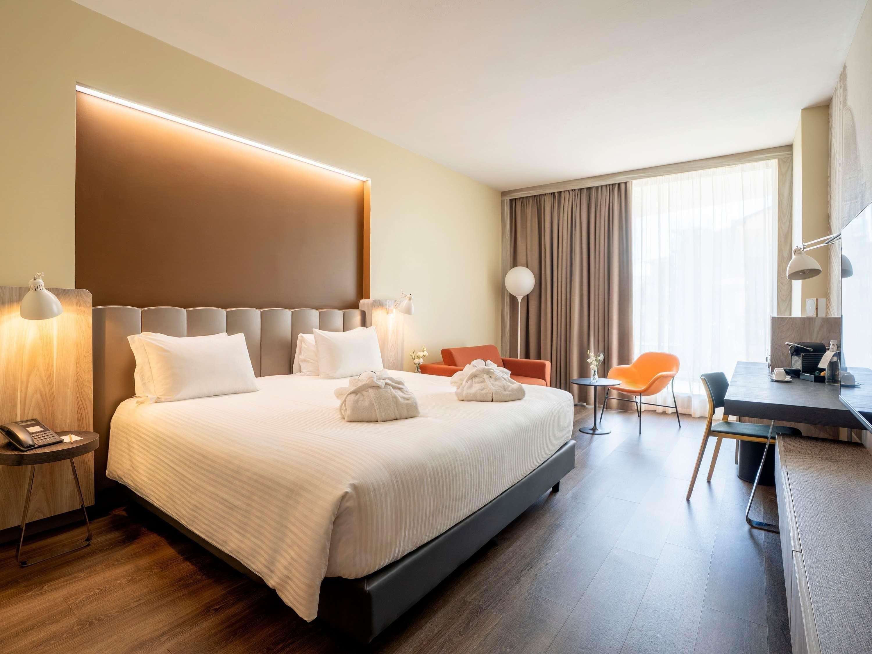 Une chambre d’hôtel avec un grand lit, des lampes de chevet, un bureau avec une chaise et une vue sur l’extérieur.