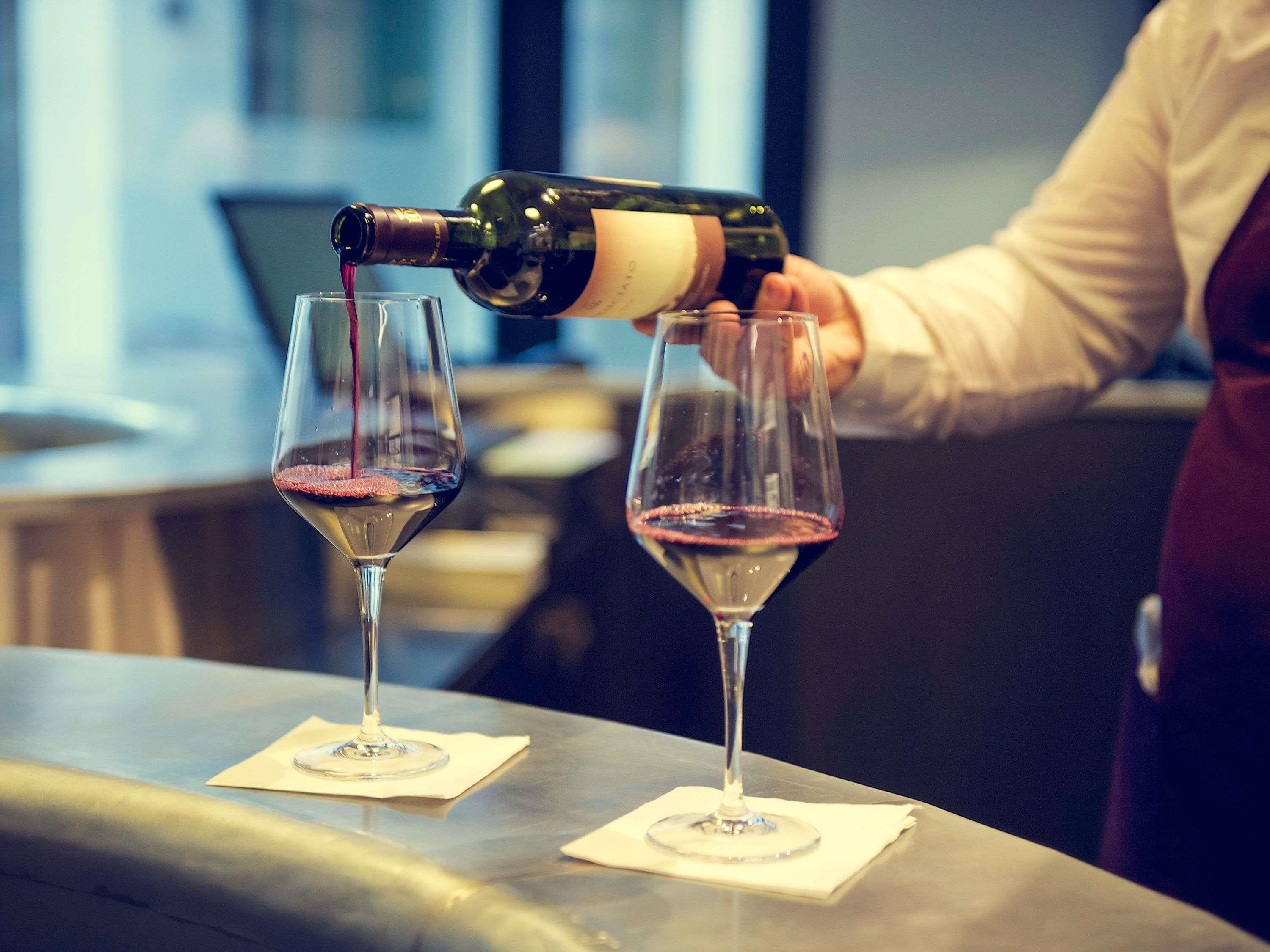 A person pouring wine into two glasses on a bar counter.
