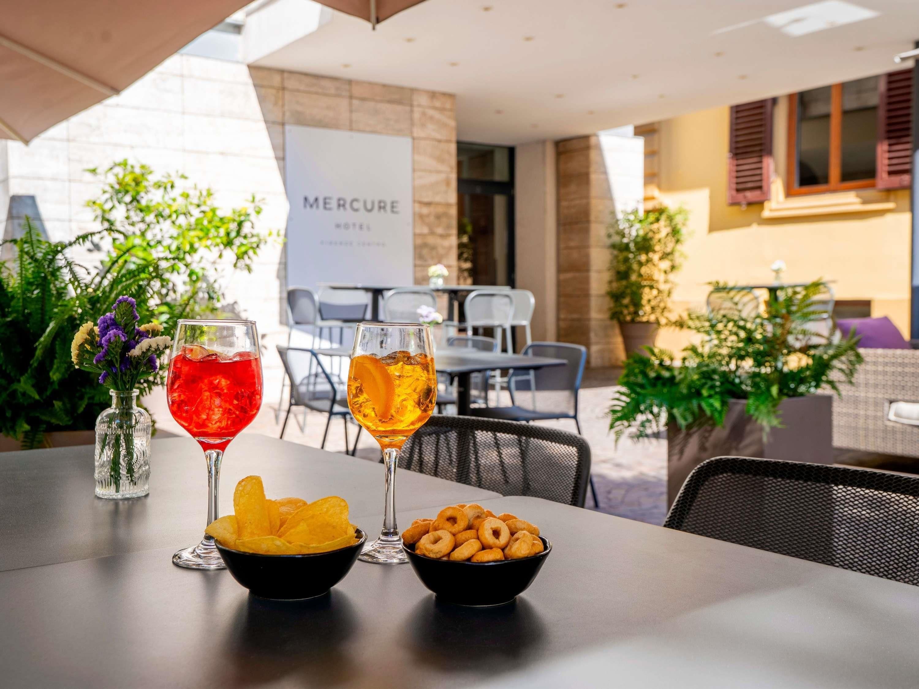 A table with two drinks, a bowl of chips, and a bowl of doughnuts, with a 'Mercure Hotel' sign in the background.