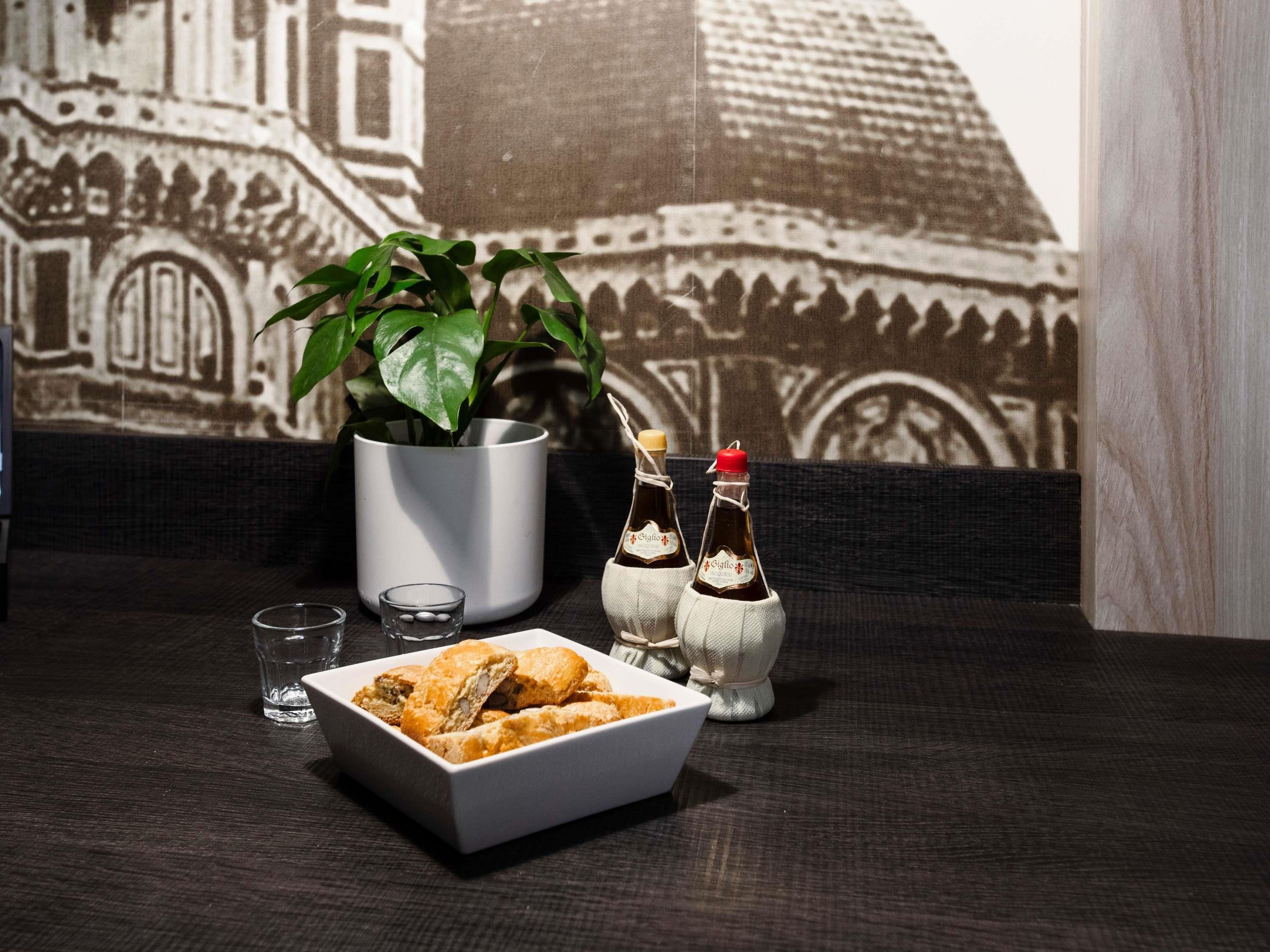 Una mesa de comedor con un tazón blanco de comida frita, dos botellas pequeñas de salsa, un vaso y una planta en maceta.