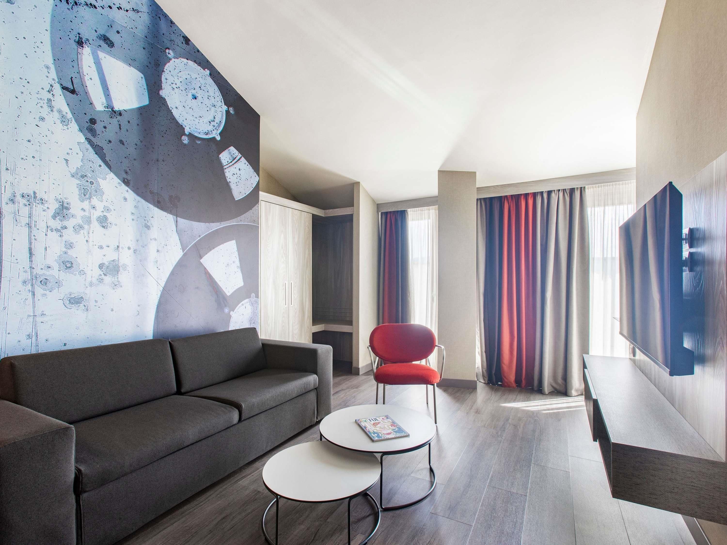 A modern living room with a grey sofa, a red chair, a small white table, and a large abstract wall mural.