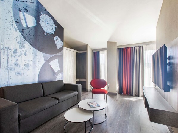 A modern living room with a grey sofa, a red chair, a small white table, and a large abstract wall mural. - Mercure Firenze Centro (Florence)