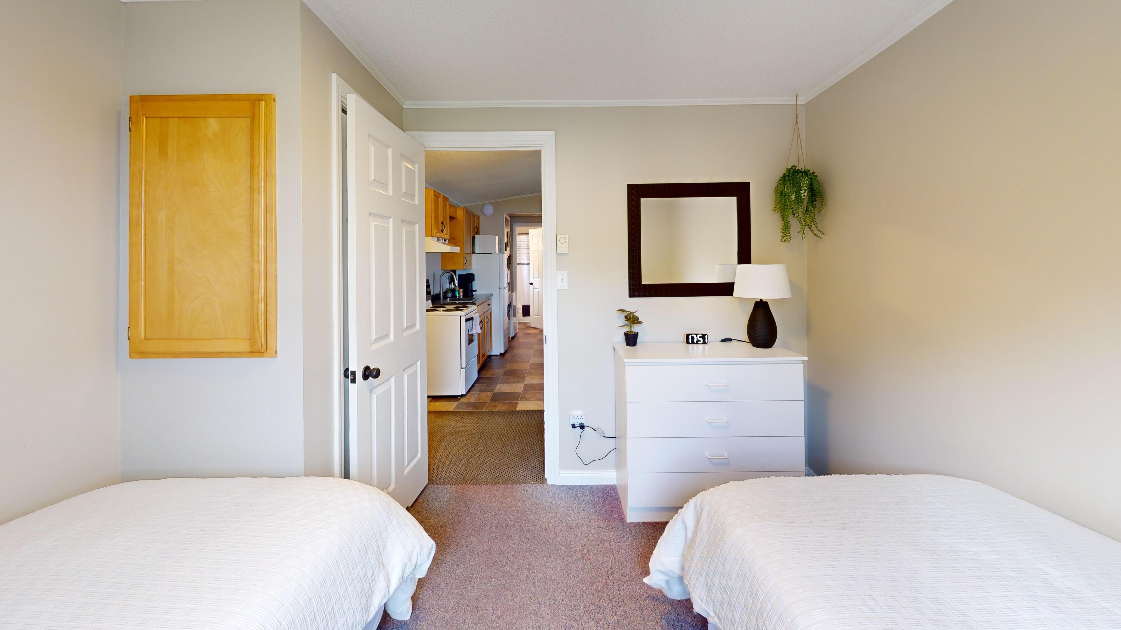 A hotel room with two beds, a dresser, a mirror, a lamp, and a potted plant.