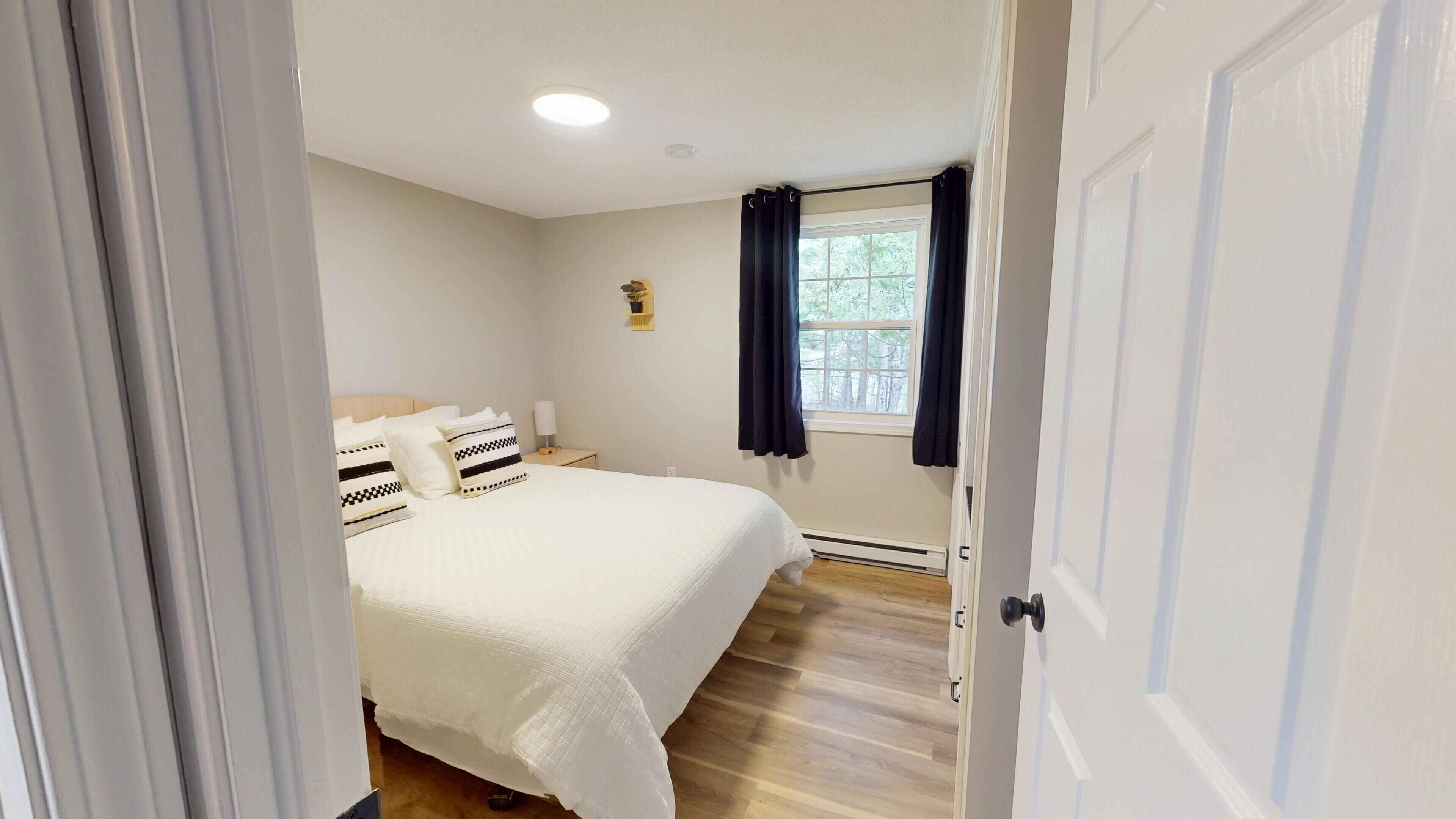 A bedroom with a bed, a nightstand, a window with curtains, and a small plant on the wall.
