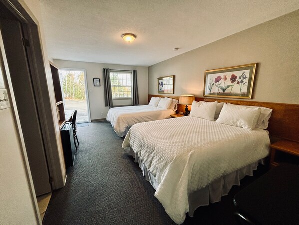 A hotel room with two beds, a desk, and a chair. There is a window with curtains, a painting on the wall, and a ceiling light. - Lakeside Stays (Plaster Rock)