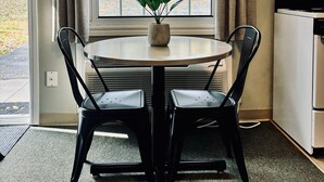 Un coin repas avec une table ronde, deux chaises, une plante en pot et une fenêtre avec des rideaux.
