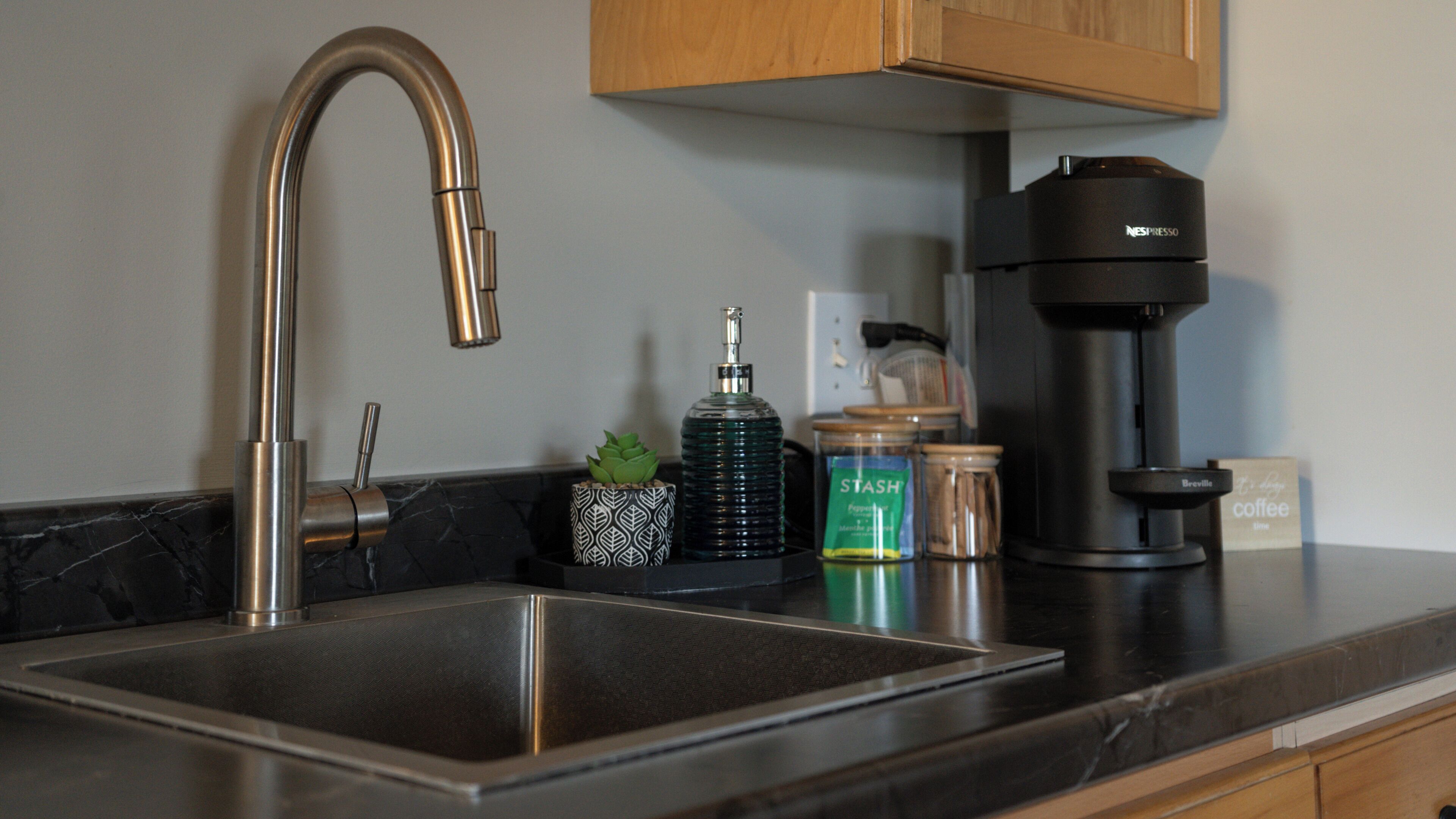 A kitchen with a modern stainless steel sink, a coffee maker, and various kitchen items on the counter.