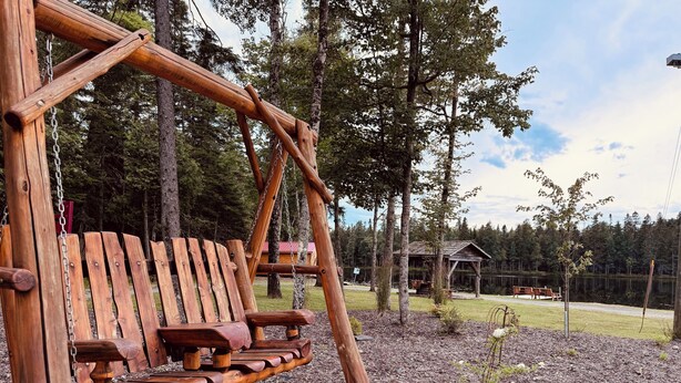 Un ensemble de balançoires en bois installé dans un espace boisé, avec une cabane en arrière-plan.