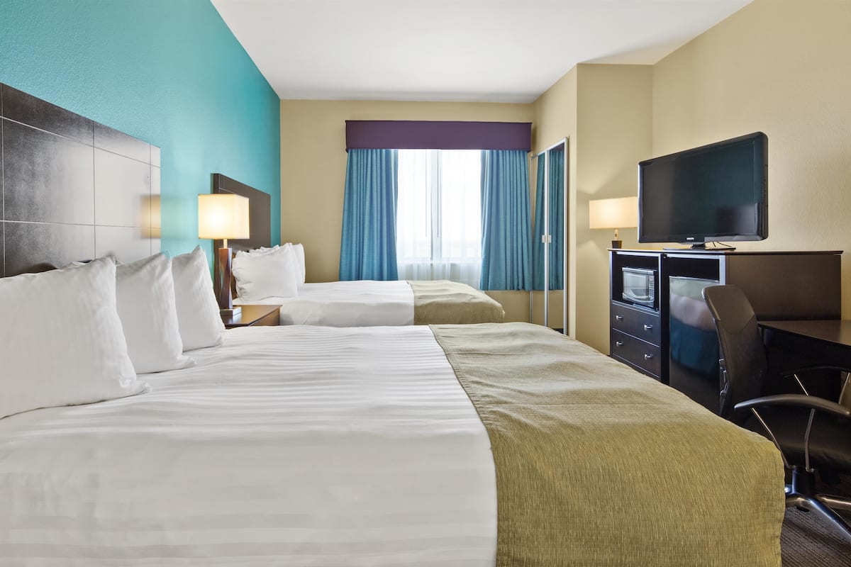 Ein Hotelzimmer mit zwei Betten, einem Schreibtisch, einem Fernseher, einer Mikrowelle und einem Sessel.