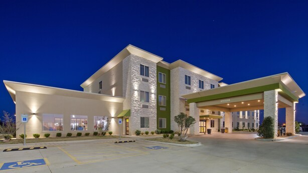 Un hotel de varios pisos con entrada cubierta, estacionamiento con espacios para discapacitados y un cielo despejado por la noche.
