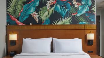 A hotel room with a bed, two bedside lamps, and a tropical leaf-patterned headboard.