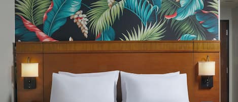 A hotel room with a bed, two bedside lamps, and a tropical leaf-patterned headboard.