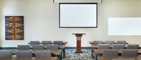 Ein Konferenzraum mit einem Rednerpult, einer großen Leinwand und Reihen von Stühlen.