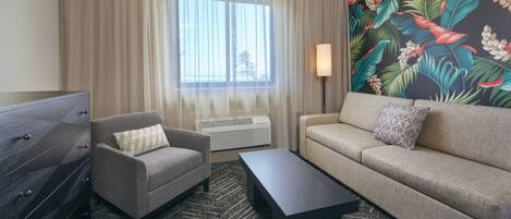 A hotel room with a sofa, armchair, and a flat-screen TV.