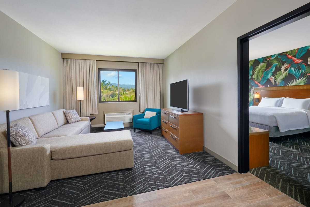 A hotel room with a sofa, a desk, a chair, a TV, and a bed.