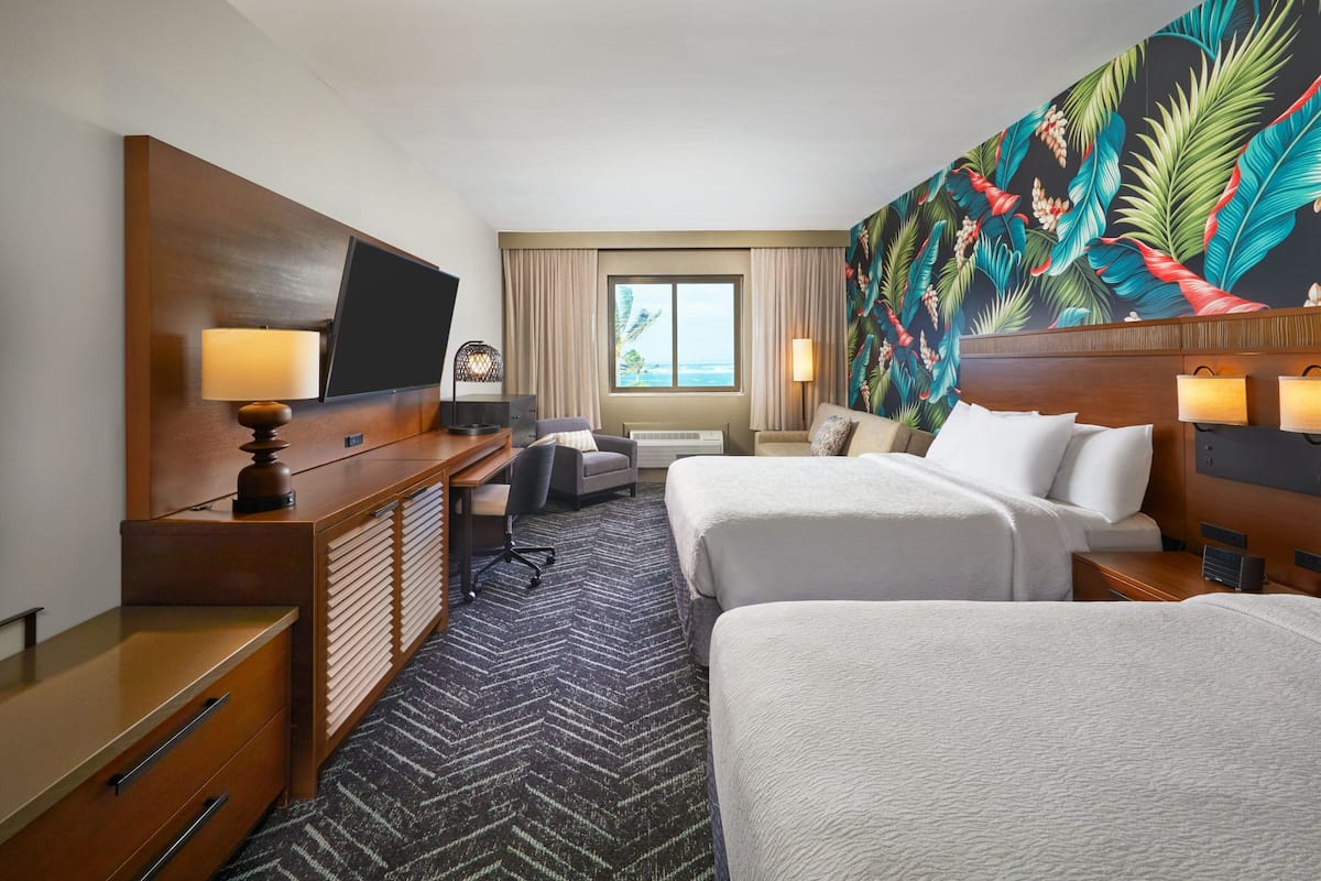 Une chambre d’hôtel avec deux lits, un bureau avec une chaise, une télévision et une grande fenêtre avec des rideaux.