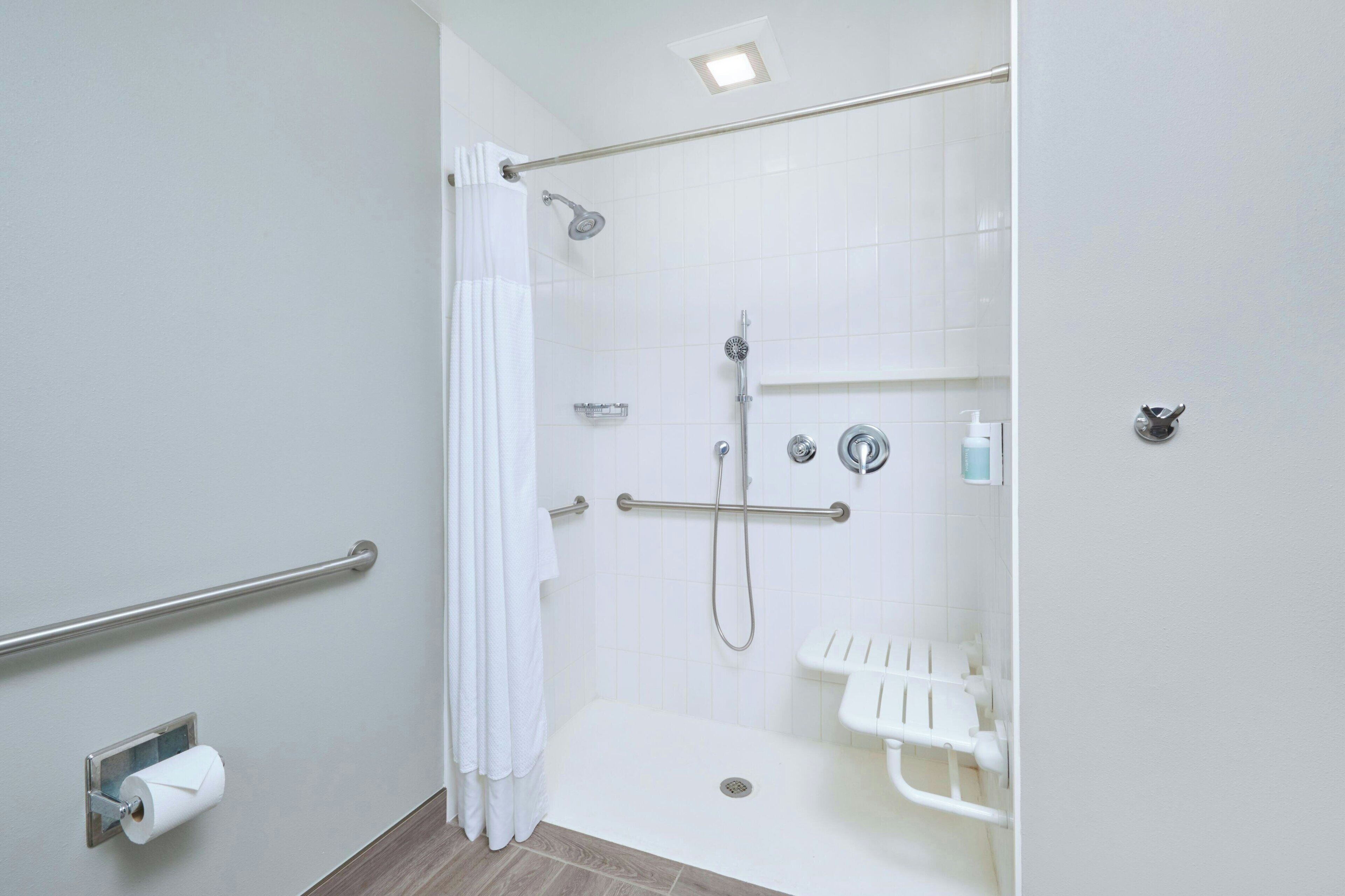 A modern bathroom with a walk-in shower, grab bars, a toilet paper holder, and a hand dryer.