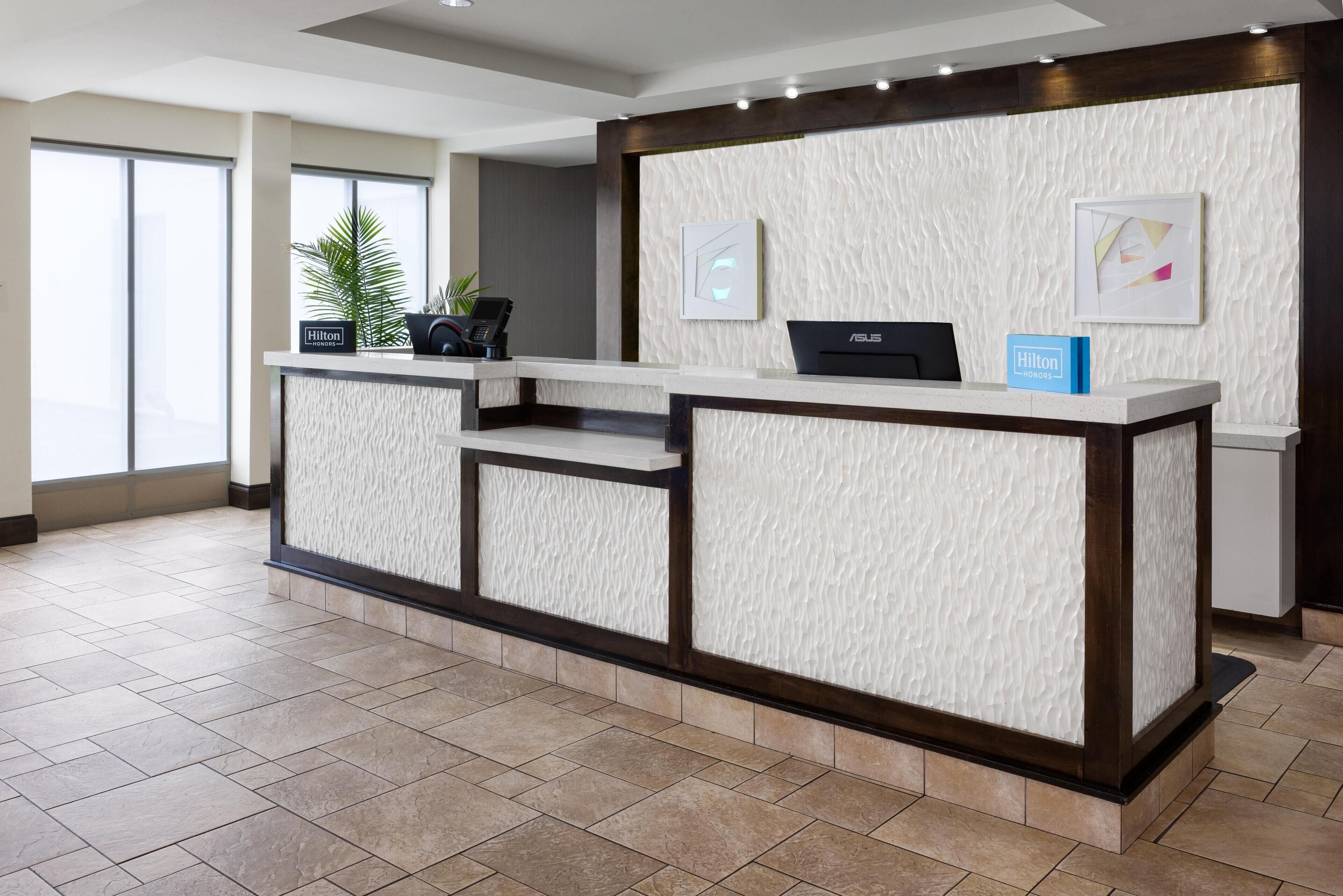 A hotel reception desk with a modern design, a digital screen, and a blue sign indicating the hotel name.