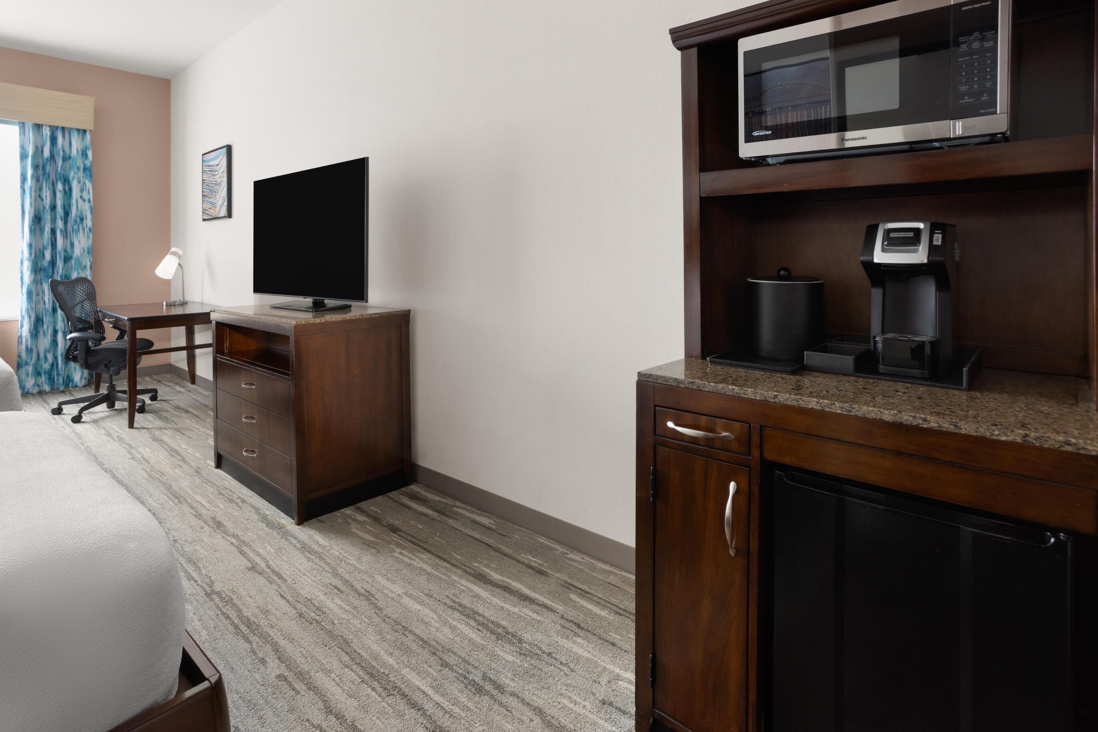 A hotel room with a bed, a desk with a computer, a television, a microwave, and a coffee maker.