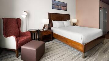 Quarto de hotel com uma cama grande, uma poltrona vermelha, uma mesa pequena e um abajur.