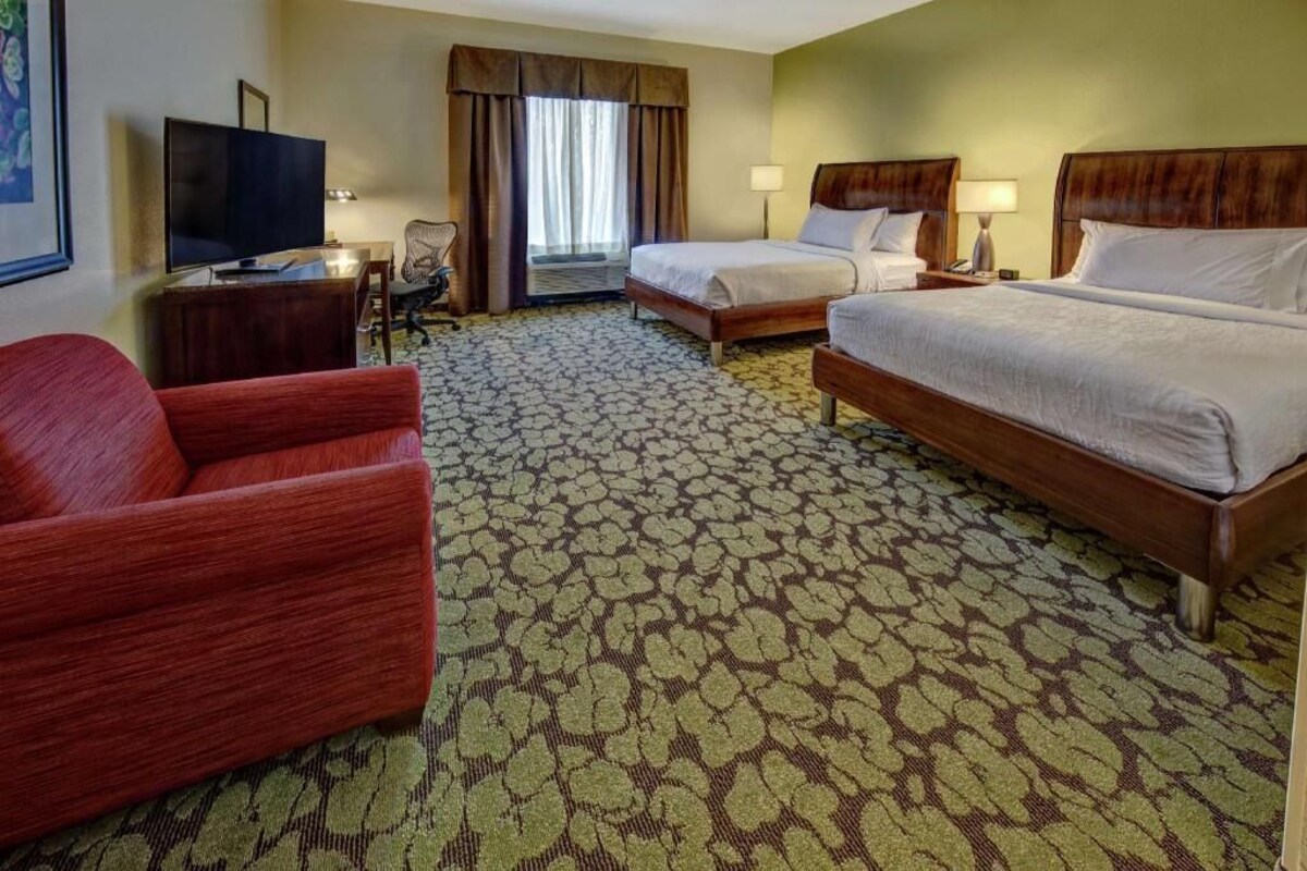 A hotel room with two beds, a TV, a desk, and a red armchair.