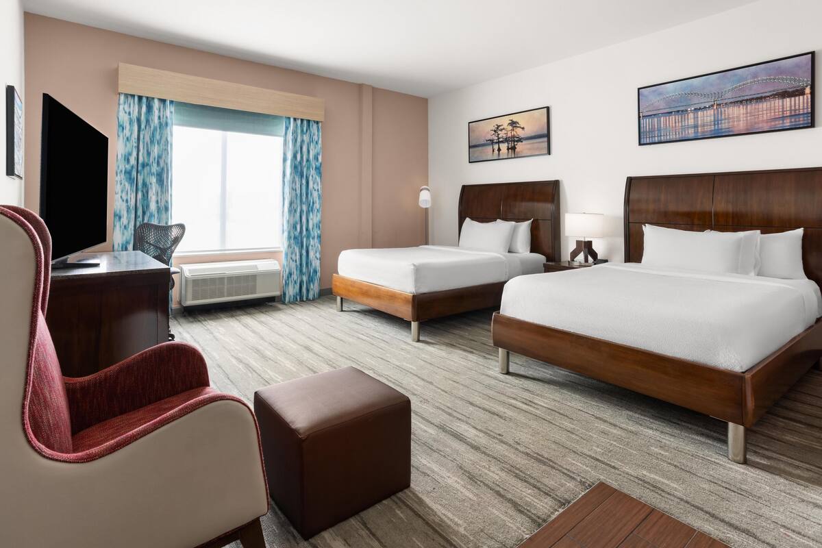 A hotel room with a large bed, two smaller beds, a desk, a chair, and a television.