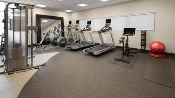 A gym with treadmills, elliptical machines, a squat rack, and a red exercise ball.